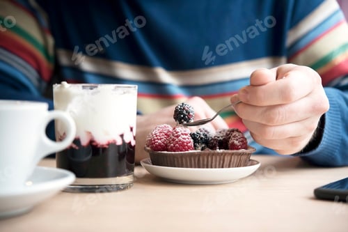 Preview: Man in a cozy cafe, drinking a latte, eating a cake made of ripe raspberries and blackberries