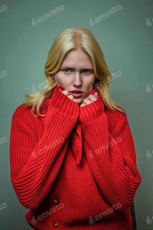 Preview: Young woman in a cozy red sweater with a serious expression against a soft green background