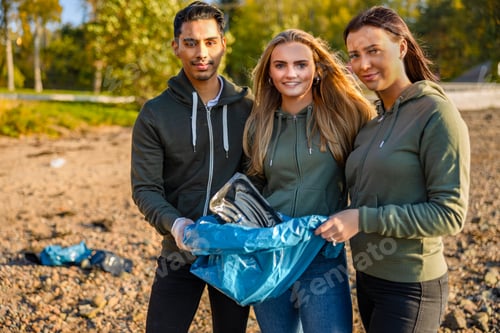 Preview: Smiling team of volunteers holding garbage bag at beach