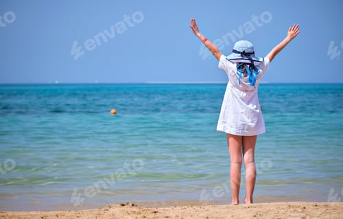 Preview: Rear view of child girl in white dress and hat standing barefoot with arms raised up