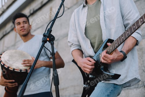 Preview: Young happy male buskers playing guitar and djembe at city street