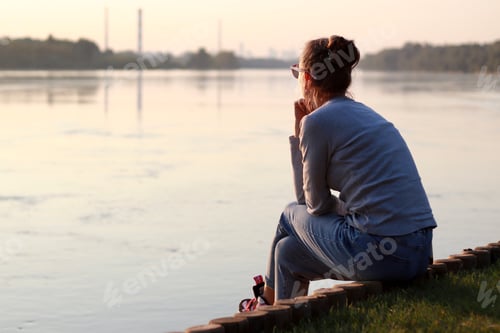 Preview: Young woman is sitting by the river bank and thinking. Sitting alone, deep thinking.