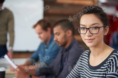 Preview: Portrait of an attractive young woman sitting in an office with colleagues in the background