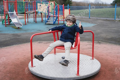 Preview: portrait active school kid playing in park,Happy boy sitting on merry go round in playground