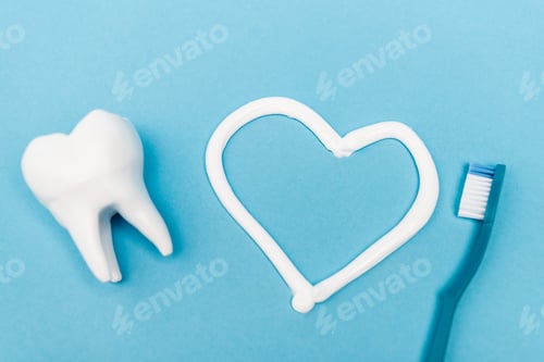 Preview: Top view of tooth model, heart sign from toothpaste and toothbrush on blue background