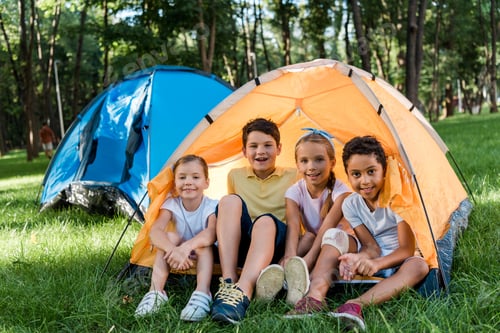 Preview: happy multicultural kids smiling while sitting in yellow camp