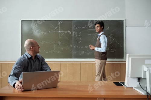 Preview: Mixed-race student standing by blackboard and looking at teacher
