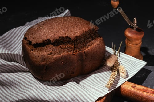 Preview: Freshly baked brown rye bread on wooden cutting board on black background