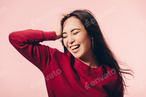 Preview: attractive asian woman in red sweater with closed eyes smiling isolated on pink