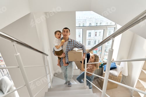 Aperçu: Happy family with kid son carrying boxes going upstairs arriving into new home.