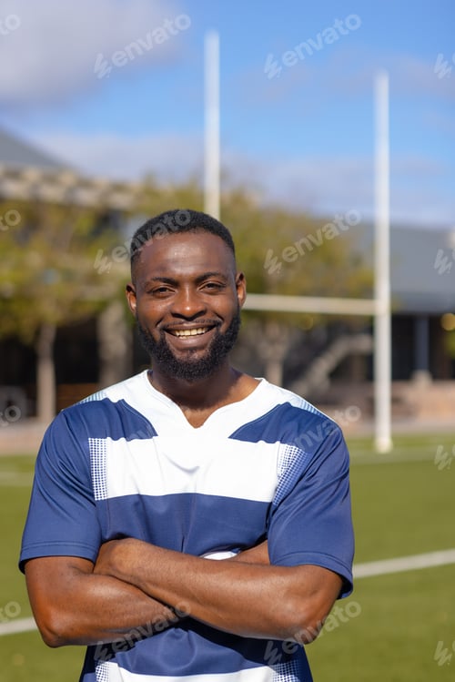 Preview: African American young male athlete standing on a rugby field, smiling at camera, copy space