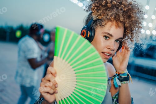Preview: Young woman wearing headphones and holding a fan at music festival