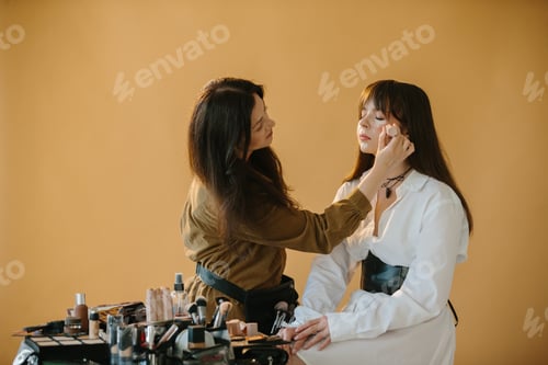 Preview: Behind-the-Scenes: Makeup Artist Prepares Model for Photoshoot in Studio with Beige Background