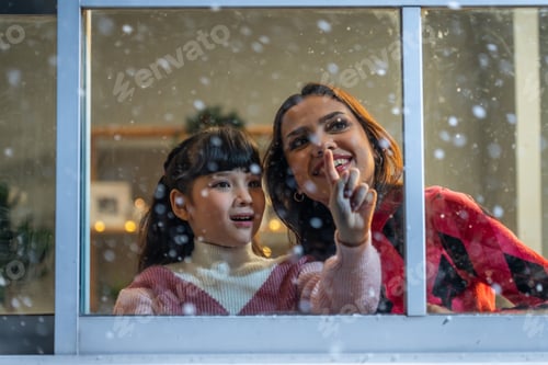 Preview: Adorable child looking at the window and admire snowflakes with mother.