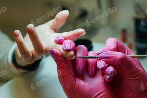 Preview: Close up of manicure master in rubber gloves applying red nails in the beauty salon.