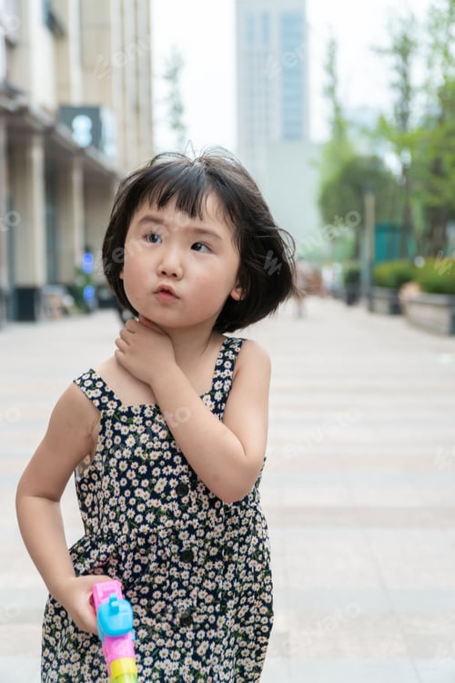 Preview: Vertical shot of an East Asian little girl playing with water gun in the street