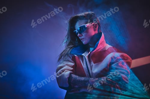 Preview: Inked attractive female posing in a neon vivid lights of a studio surrounded by smoke