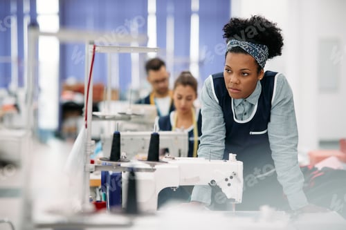 Preview: Displeased black seamstress at production line in a factory.