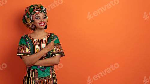 Preview: Beautiful african woman looking and pointing at copy space