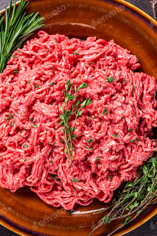 Preview: Raw mince beef and lamb meat on a rustic plate with herbs. Dark background. Top view