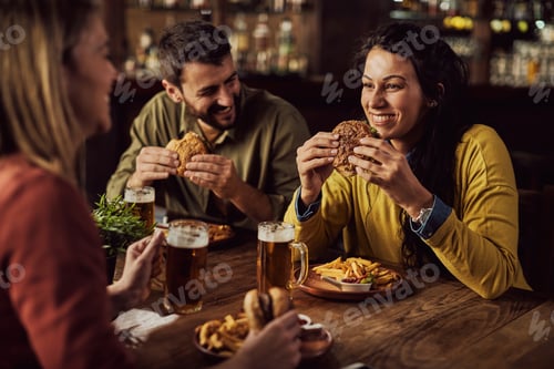 Preview: Young happy woman eating hamburgers with her friends in a pub.