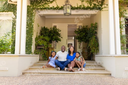 Preview: Sitting on porch steps, happy family of four with daughters smiling and enjoying time together