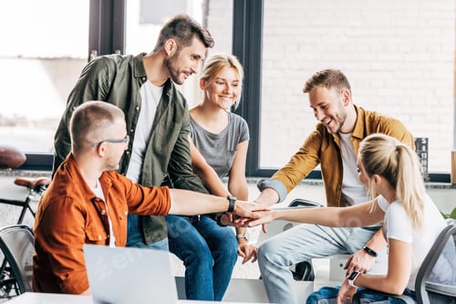 Preview: group of happy young entrepreneurs making team gesture while working on startup together at office