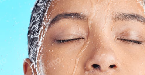 Preview: But firstskincare. Studio shot of a young woman taking a shower against a blue background.