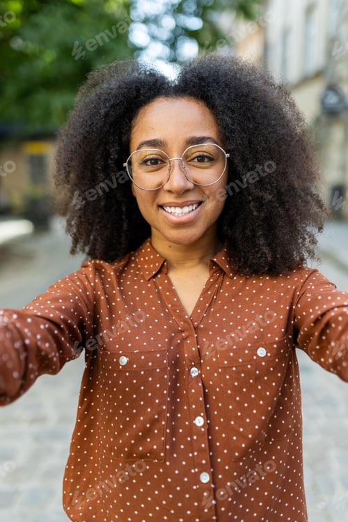 Preview: Vertical close-up photo of a young smiling African-American woman with curly hair, wearing glasses