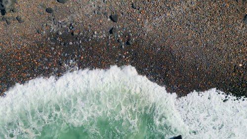Preview: Aerial view beautiful waves rolling on seashore with dark stones. Ocean foaming