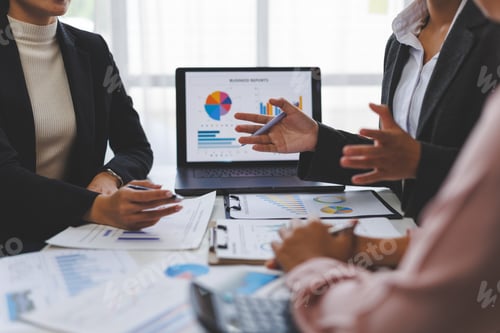 Preview: Business people analyzing charts on laptop and documents in office meeting