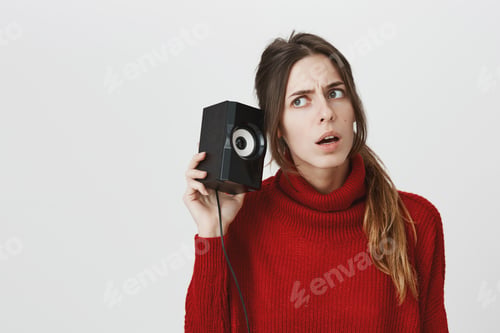 Preview: Horizontal shot of young woman with ponytail in red sweater frowns keeps musical column behind ear