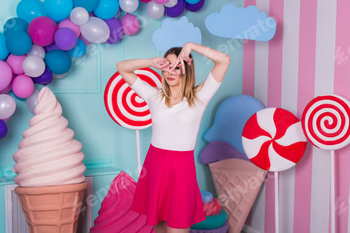 Preview: Portrait of woman in pink dress on background decorated with huge candies and ice cream.