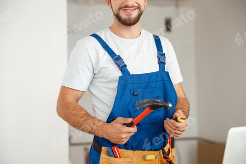 Preview: Cropped shot of professional handyman worker in uniform smiling at camera and holding hammer during