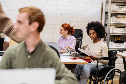 Preview: Multiracial coworkers working in office with disabled colleague in wheelchair