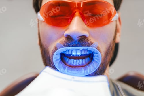 Preview: Bearded man , patient whitening teeth in modern dental clinic. Teeth treatment, health care