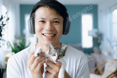 Preview: young man wearing headphones and playing with a cat.