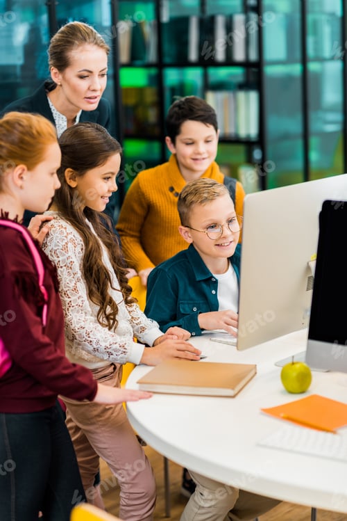 Preview: cute schoolchildren and librarian using computer together in library