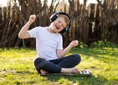 Preview: a boy with headphones listening to music on a mobile tablet and relaxing in the fresh air in nature