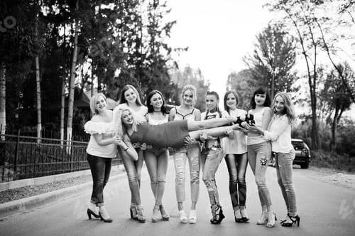 Preview: Crazy company of bridesmaids holding bride in red dress in the park at bachelorette party.