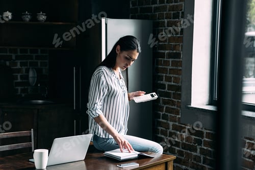 Preview: sad young woman with calculator counting tax on kitchen at home