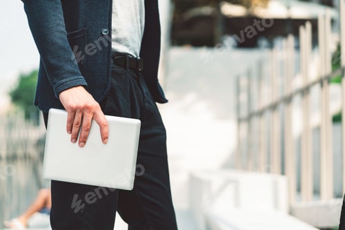 Preview: Waist down unrecognizable man side view holding a digital tablet in his hand outside
