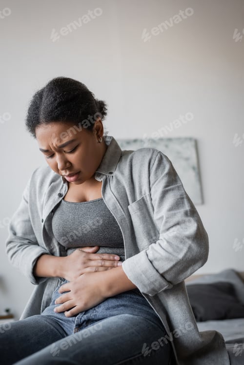 Preview: Upset multiracial woman having abdomen pain on bed at home