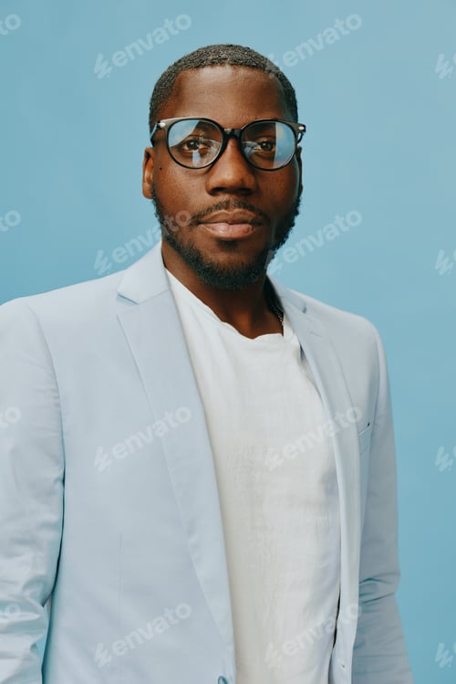 Preview: Stylish man in light blue suit with glasses, confident expression against blue background