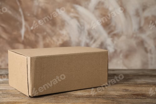 Preview: Closed cardboard box on wooden table against brown background