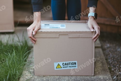 Preview: Person resting his arms on a cardboard box with a label "caution heavy package " on it
