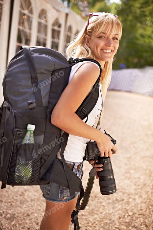 Preview: A beautiful young photographer walking with gear on her back and camera in her hands