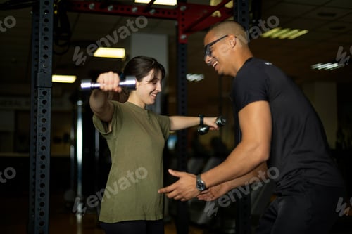 Visualização: Mulher sorridente levanta halteres com a ajuda do treinador na academia