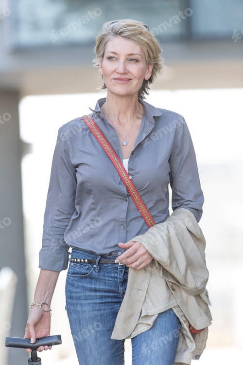 Preview: Mature woman leaving hotel with wheeled suitcase