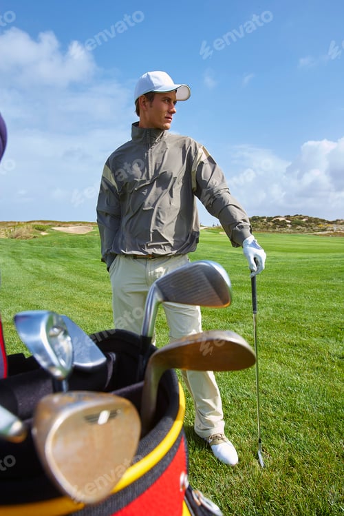 Preview: Golfer holding gold club, hand in pocket, looking away
